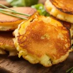 Golden brown potato pancakes stacked with a side of sour cream and chives on a wooden serving board.